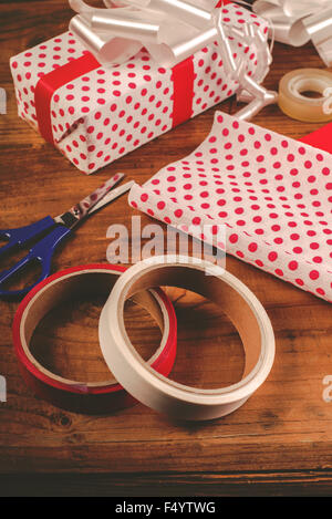 Des cadeaux de Noël et emballage décoratif présente, polka dotted papier, ciseaux et ruban bandes sur un bureau en bois, tons rétro Banque D'Images