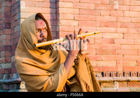 Jeune homme jouant de la flûte au burning ghats près de temple de Pashupatinath Banque D'Images