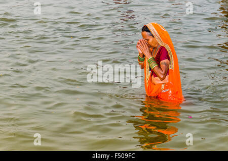 Femme en sari orange et baignoire en priant dans l'eau du Gange tôt le matin au sangam, le confluent de la riv Banque D'Images