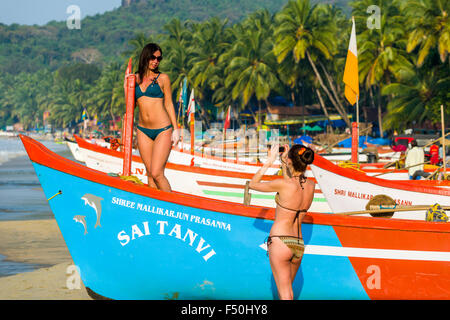 Deux jeunes femmes, portant des bikinis, prenons des photos de l'autre en face d'un bateau de pêche à la plage de Palolem Banque D'Images