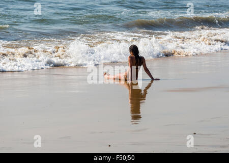 Une jeune femme portant bikini est assis dans le sable de plage d'Anjuna, face à l'entrée des vagues Banque D'Images