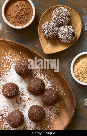 Rhum coco balls étant recouvert de noix de coco râpée sur plaque de bois, d'ingrédients (poudre de cacao, cookies) sur le côté Banque D'Images