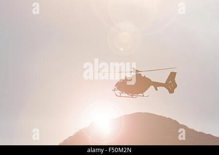 Vol en hélicoptère de sauvetage en montagne en face d'une montagne et soleil derrière elle Banque D'Images