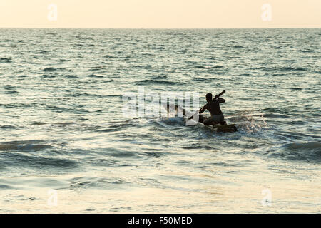 Un pêcheur est paddeling out à la mer ouverte sur son petit bateau Banque D'Images
