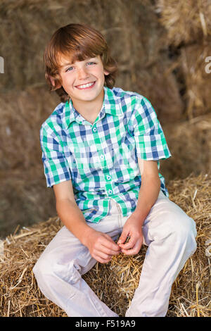 Young happy smiling boy portant une chemise à carreaux et assis dans grange sur les balles de foin ou de paille Banque D'Images