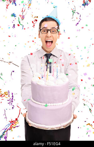 Shot vertical d'un jeune homme tenant un joyeux anniversaire gâteau et regardant la caméra de confettis serpentins voler autour de lui Banque D'Images