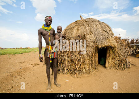 Jeune femme Nyangatom avec bébé dans les bras, se tient à côté de sa cabane de chaume. Vallée de l'Omo, Ethiopie Banque D'Images