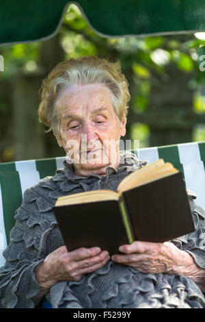 Vieille femme lisant un livre tout en restant assis dans un pavillon d'été. Banque D'Images