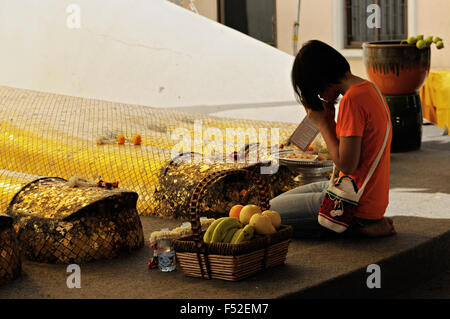 Jeune femme priant au pied des 32 mètres de haut standing statue de Bouddha de Wat Intharawihan, Bangkok, Thaïlande Banque D'Images