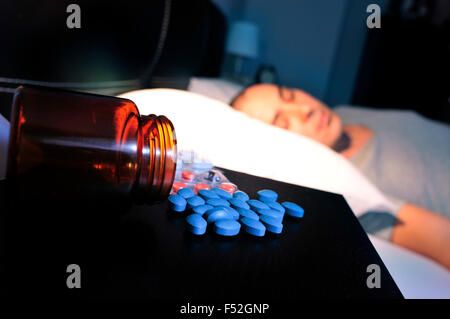 Quelques gros plan de différentes pilules dans la table de nuit et d'un jeune homme portant au lit avec ses yeux fermés, la nuit Banque D'Images