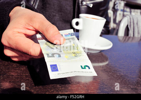 Libre d'un jeune homme avec une tasse de café de payer la note à la terrasse d'un café avec un billet de cinq euros Banque D'Images