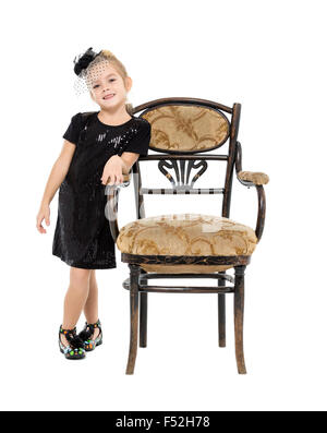 Petite fille debout près de chaise ancienne, sur fond blanc Banque D'Images