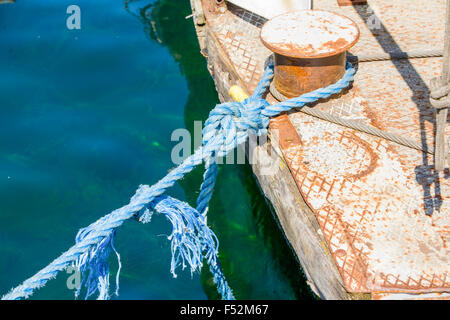 Une vue rapprochée d'une corde bleue effilochée attachée dans un nœud autour d'une borne en métal rouillé sur un quai en bois altéré. La corde montre des signes d'usure avec des extrémités effilochées, et la borne est fortement corrodée avec Banque D'Images
