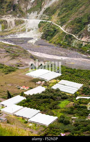 Une photographie aérienne montre un groupe de serres au toit blanc situées dans une vallée entourée de végétation verdoyante et de collines. Adjacent aux serres se trouve une grande zone aride avec de la terre exposée Banque D'Images