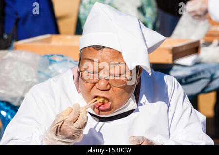 Le Japon. Omochi, riz bashing festival. Grand Senior woman sitting japonais omochi, et manger du riz cuit avec des baguettes. Close up, la tête et les épaules. Banque D'Images