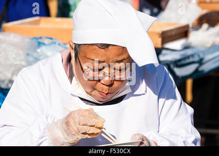 Le Japon. Omochi, riz bashing festival. Grand Senior woman sitting japonais omochi, et manger du riz cuit avec des baguettes. Close up, la tête et les épaules. Banque D'Images