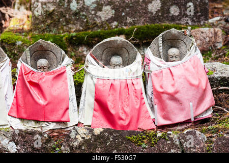 Le Japon, Koyasan, Okunoin cemetery. Trois Jizo bosatsu pierre-statue avec bavettes sur rouge, disposées en ligne sur pierre avec un peu plus de mousse derrière. Banque D'Images