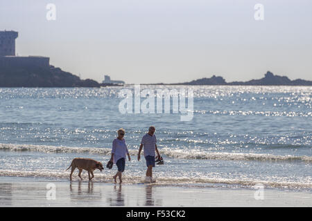 Couple walking dog sur mer à St Ouen's beach Jersey avec La Rocco Tower dans l'arrière-plan Banque D'Images