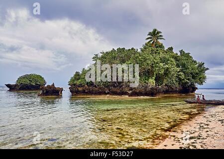 L'île de Kiriwina garçons local avec canoë et petite île tropicale Banque D'Images