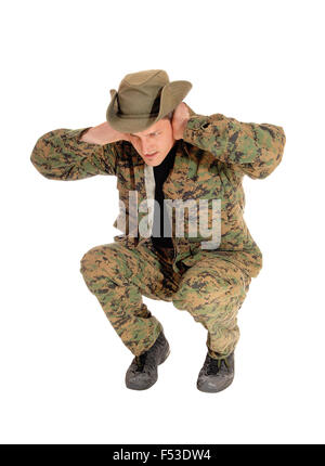 Un soldat en uniforme de camouflage accroupi sur le sol en prévision d'une explosion, isolée pour fond blanc. Banque D'Images