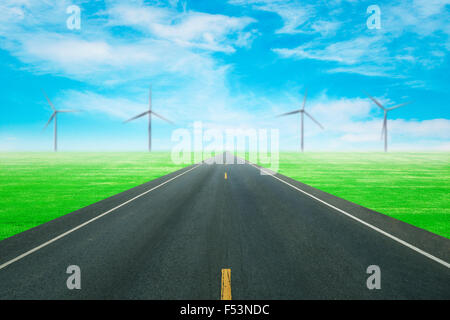 La route d'asphalte à travers le champ vert avec l'éolienne et fond de ciel bleu Banque D'Images