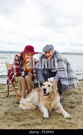 Happy senior couple avec leur chien reposant sur beach Banque D'Images