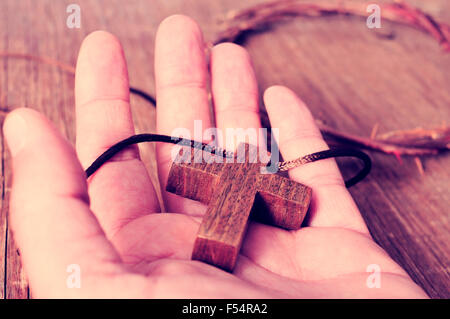 Une croix en bois dans la main d'un jeune homme et une représentation de la couronne d'Épines du Christ sur une surface en bois rustique, avec Banque D'Images