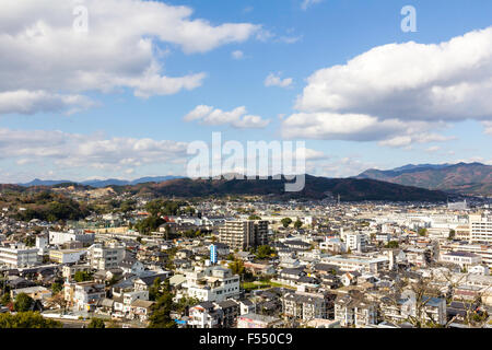 La ville de Tsuyama vu de la colline du château. La plupart des bâtiments blancs, de deux à cinq étages, avec des montagnes en arrière-plan et nuages ciel bleu. Banque D'Images