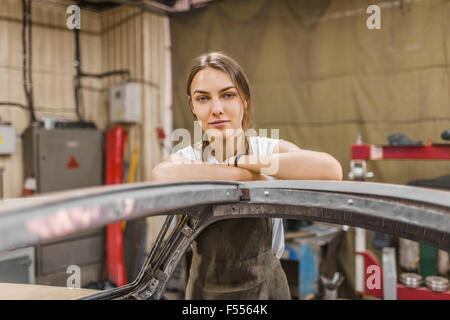 Portrait of female mechanic s'appuyant sur voiture au garage Banque D'Images