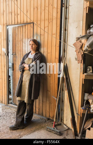 Portrait of smiling mechanic with arms crossed leaning on wooden wall au garage Banque D'Images