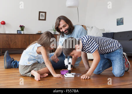 Famille heureuse à la recherche à l'aide de microscope, garçon sur plancher de bois franc Banque D'Images