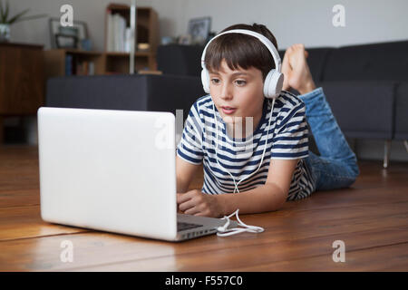 Boy listening music on headphones while using laptop at home Banque D'Images