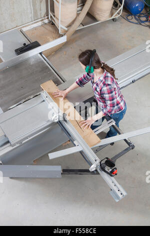 Une femme à l'aide d'un menuisier Scie sur table coulissante dans un atelier Banque D'Images