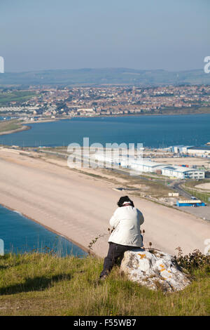 Femme assise sur le rocher et regardant la Chesil Bank et la Fleet Lagoon à Portland, Weymouth, Dorset, Royaume-Uni, en octobre Banque D'Images