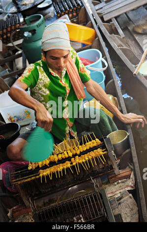 Griller les brochettes de viande de jeune homme sur un bateau à Taling Chan floating market, Bangkok, Thaïlande Banque D'Images