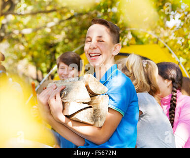 Laughing boy holding bois d'allumage sur camping Banque D'Images