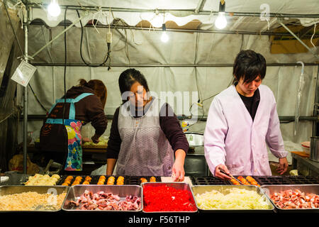 Le Japon. Kobe. La nuit. Poulpe Takoyaki, food, yatai. Deux adultes, hommes et femmes, la préparation d'Octopus balles spécialement conçus sur la plaque chaude. Banque D'Images