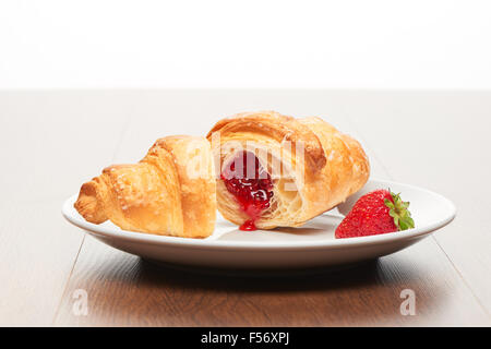 Fresh french croissant avec de la confiture de fraise coupées en deux morceaux de remplissage et de fraise sur la plaque de céramique blanche sur la lumière vive bro Banque D'Images