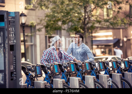 Deux hommes par un rack de location de bicyclettes dans un parc de la ville Banque D'Images