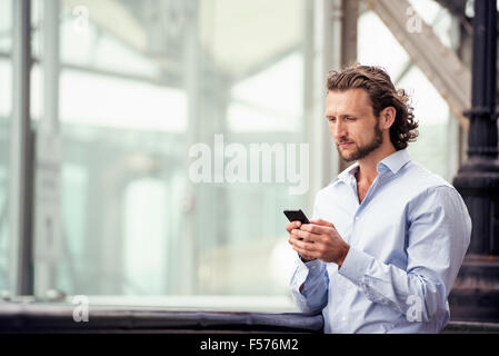 Un homme debout à l'extérieur, sur la rue, contrôler son téléphone cellulaire. Banque D'Images