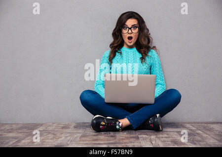 Portrait of woman sitting on the floor with laptop and looking at camera sur fond gris Banque D'Images