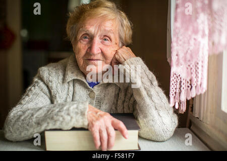 Une vieille femme assise avec un livre à la table. Banque D'Images