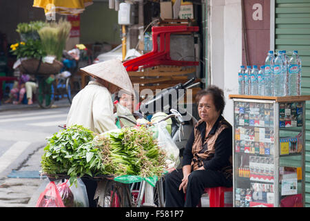 Dame vietnamienne la vente de légumes à Hanoi old quarter est arrêté près d'un distributeur automatique de cigarettes, Vietnam Banque D'Images