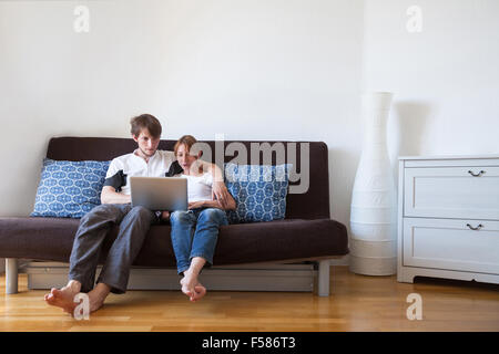 Jeune famille à l'aide d'ordinateur portable à la maison, en couple sur le canapé avec ordinateur Banque D'Images