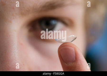 Un jeune homme s'efforce de trouver un équilibre entre une lentille de contact est sur l'index. Banque D'Images