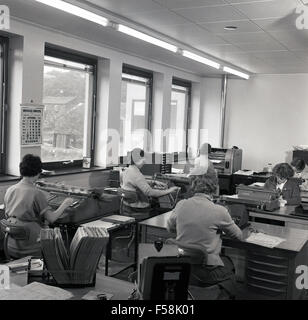 Septembre 1960, photo historique montrant les secrétaires travaillant dans un bureau, à l'aide de certains comptes à l'aide de grandes entreprises industrielles machines à écrire. Banque D'Images