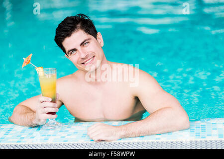 Beau jeune homme de boire un cocktail tout en vous relaxant dans une piscine Banque D'Images