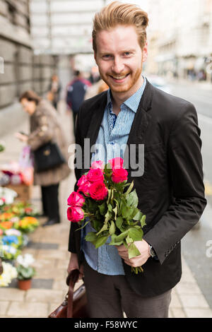 Businessman holding roses et souriant dans une ville Banque D'Images