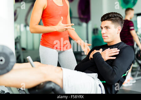 Belle jeune femme demandant à un jeune homme dans la salle de sport et d'entraînement sur son Banque D'Images