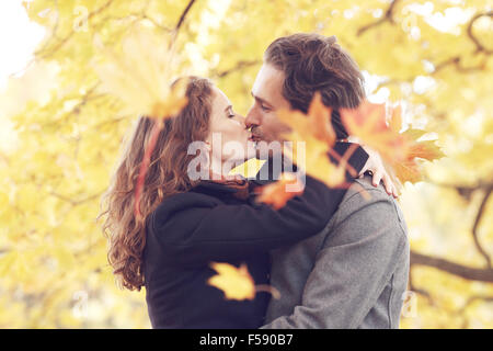 Beau couple avec feuilles d'érable kissing in autumn park Banque D'Images